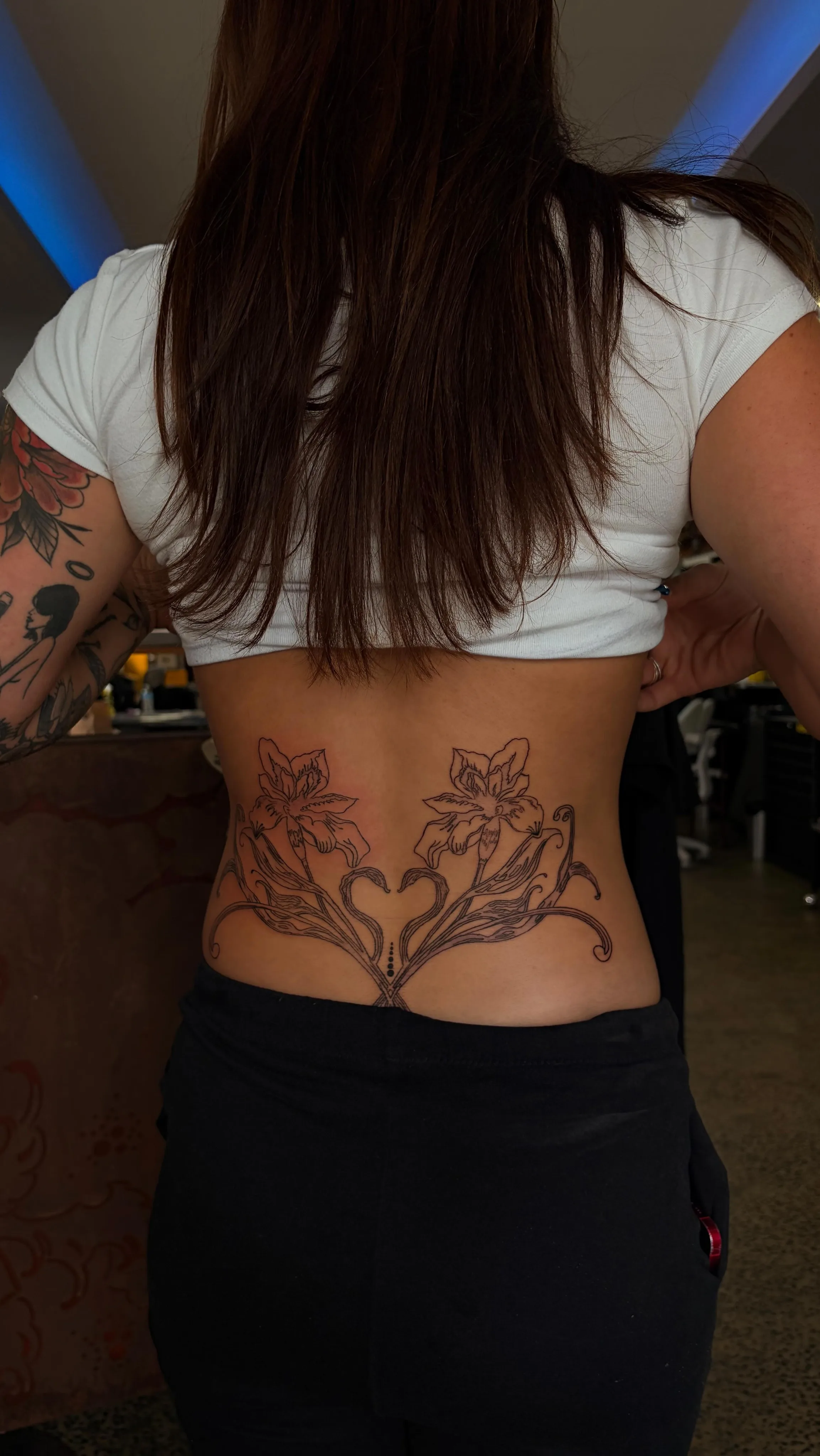 Fine-line floral lower-back tattoo with blue neon studio interior