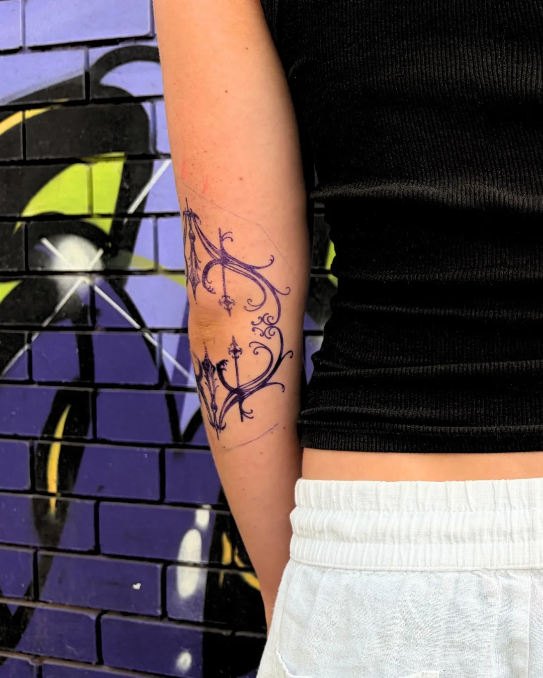 Purple-line ornamental filigree forearm tattoo