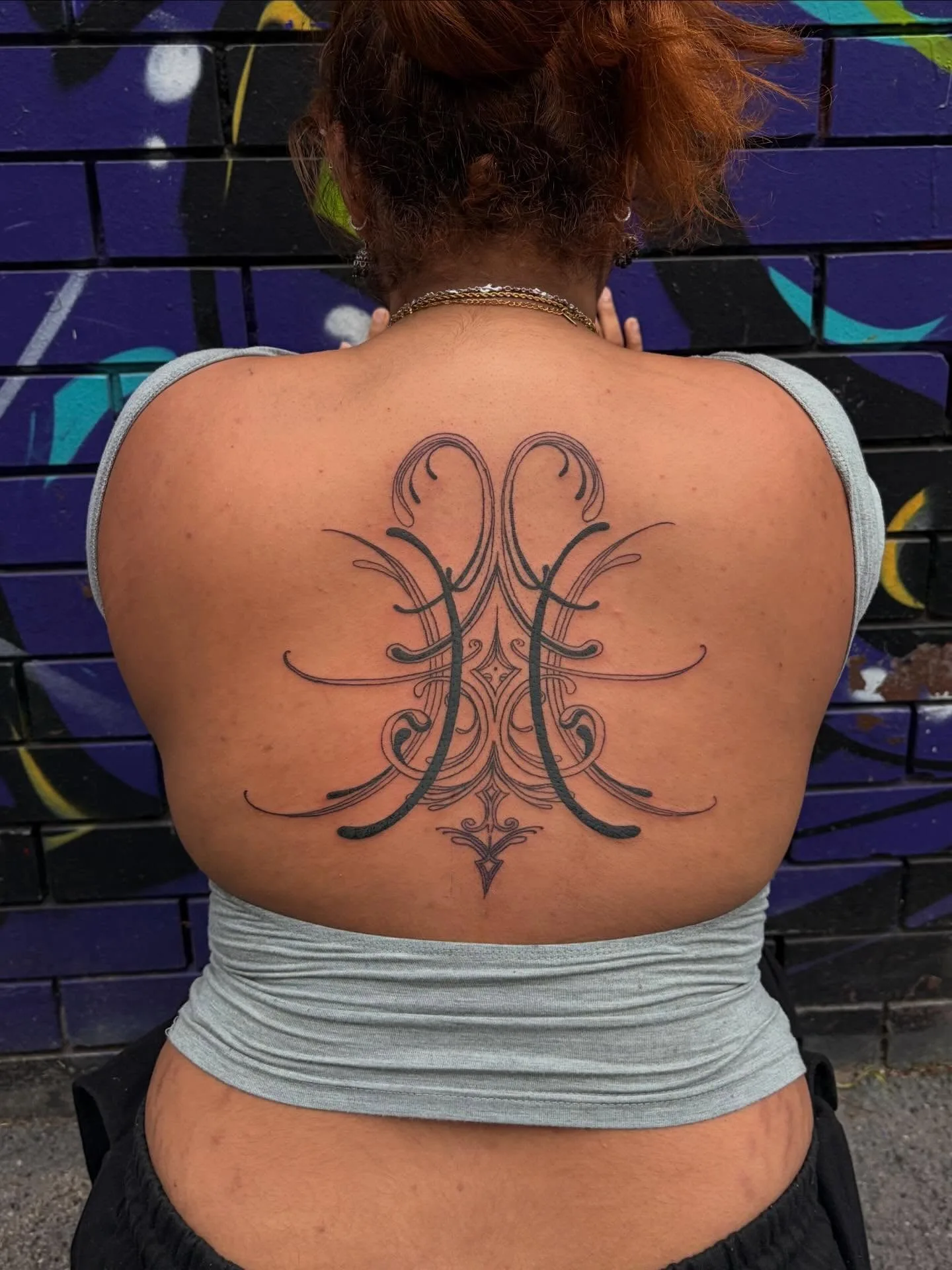 Ornamental filigree and lettering black-line back tattoo