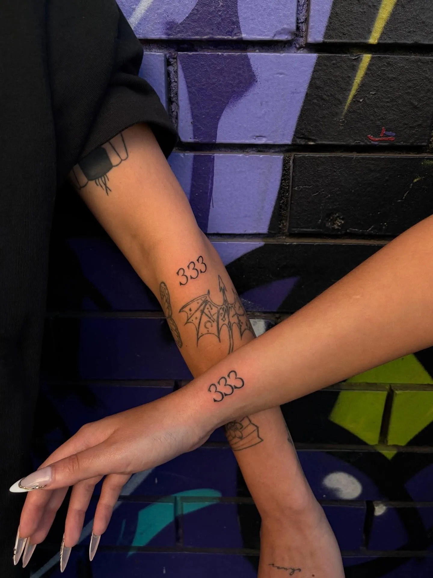 Matching fine-line 333 and bat-wing forearm tattoos