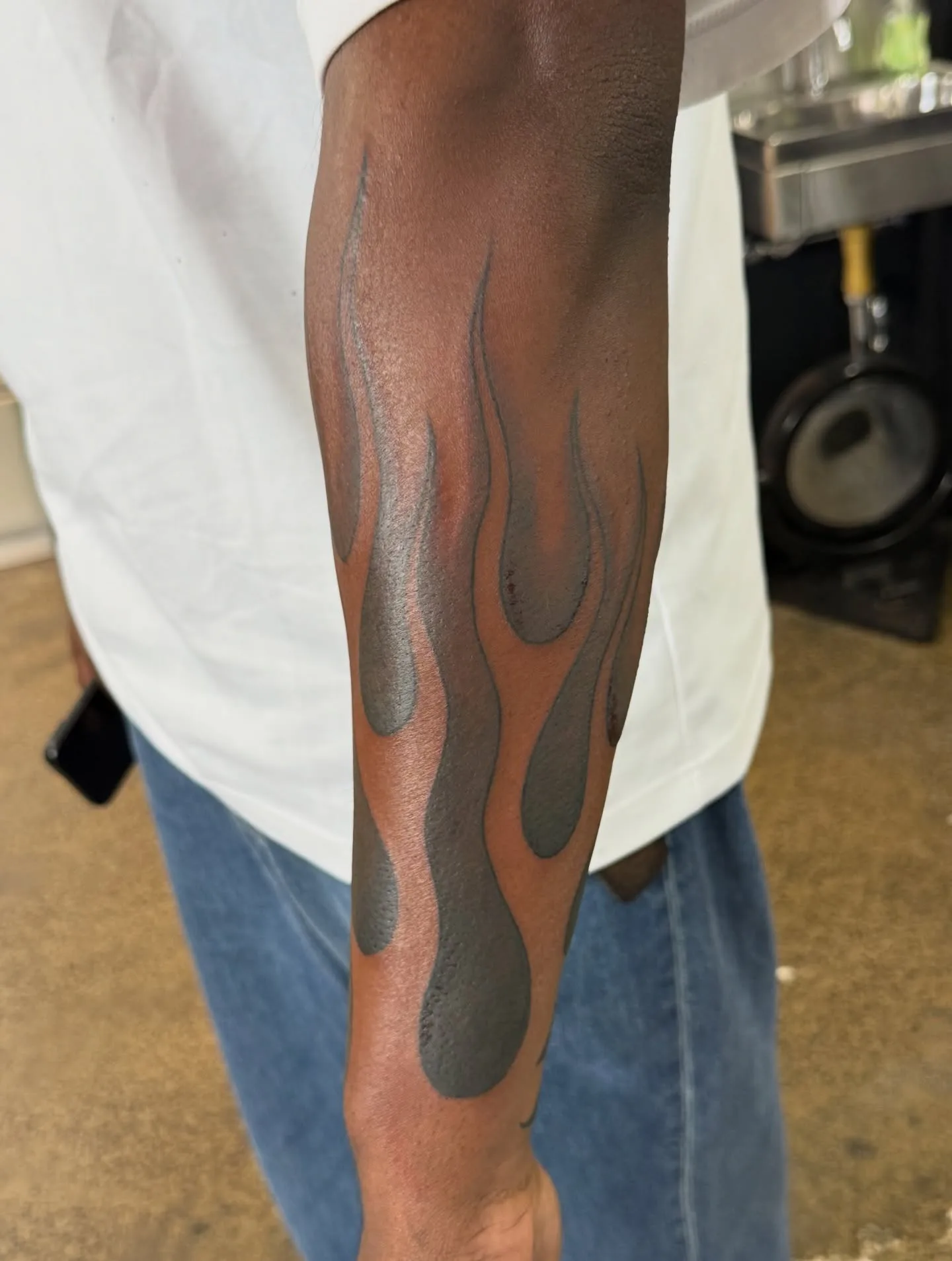 Black-and-grey flame forearm tattoo on dark skin