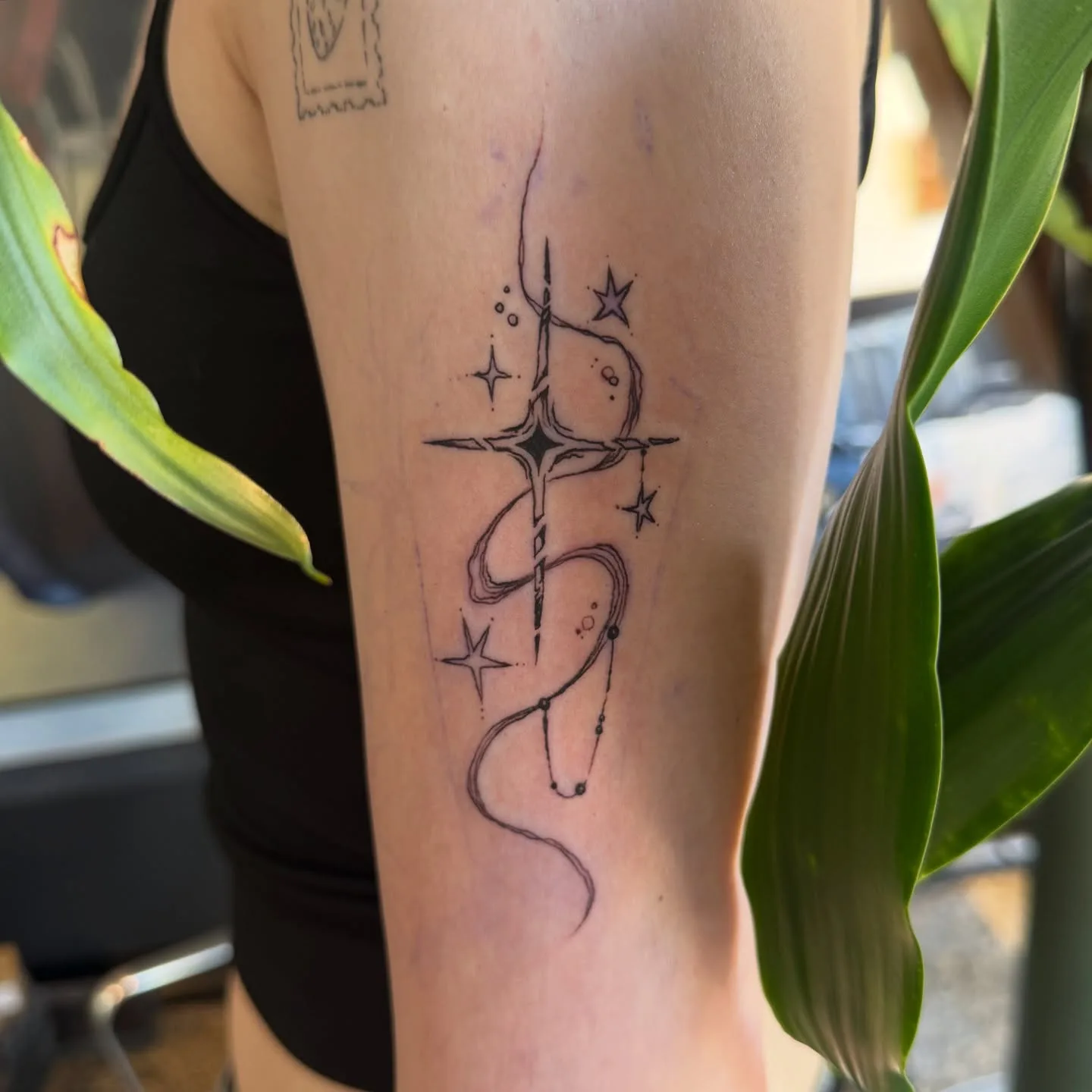 Fine-line celestial upper-arm tattoo with star and ribbon motif